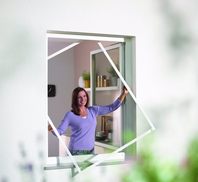 Frau setzt Insektenschutzgitter ins Fenster Insektenschutz